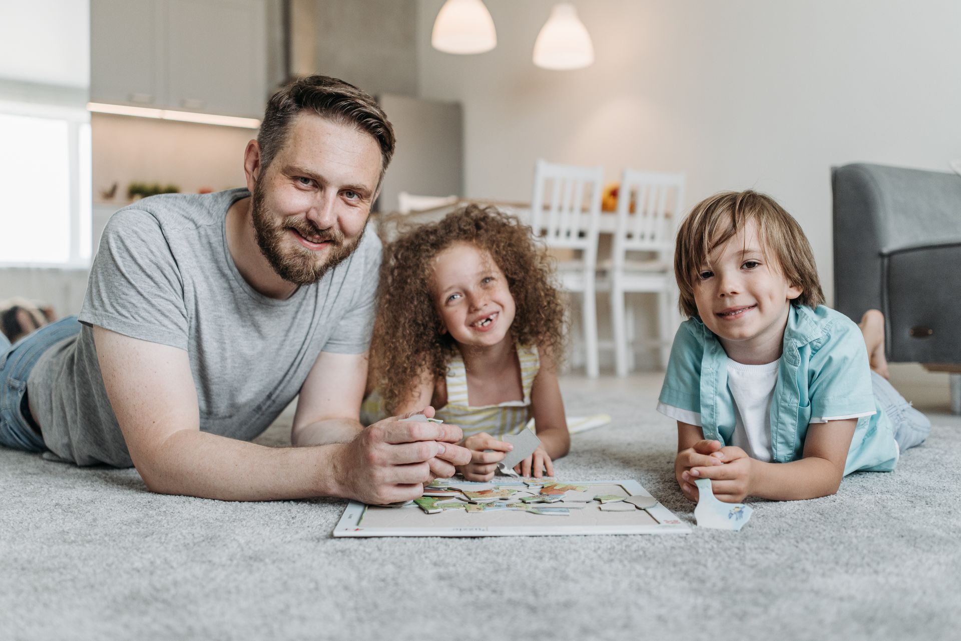 Dad lying on the living room carpet doing a puzzle with his daughter and son