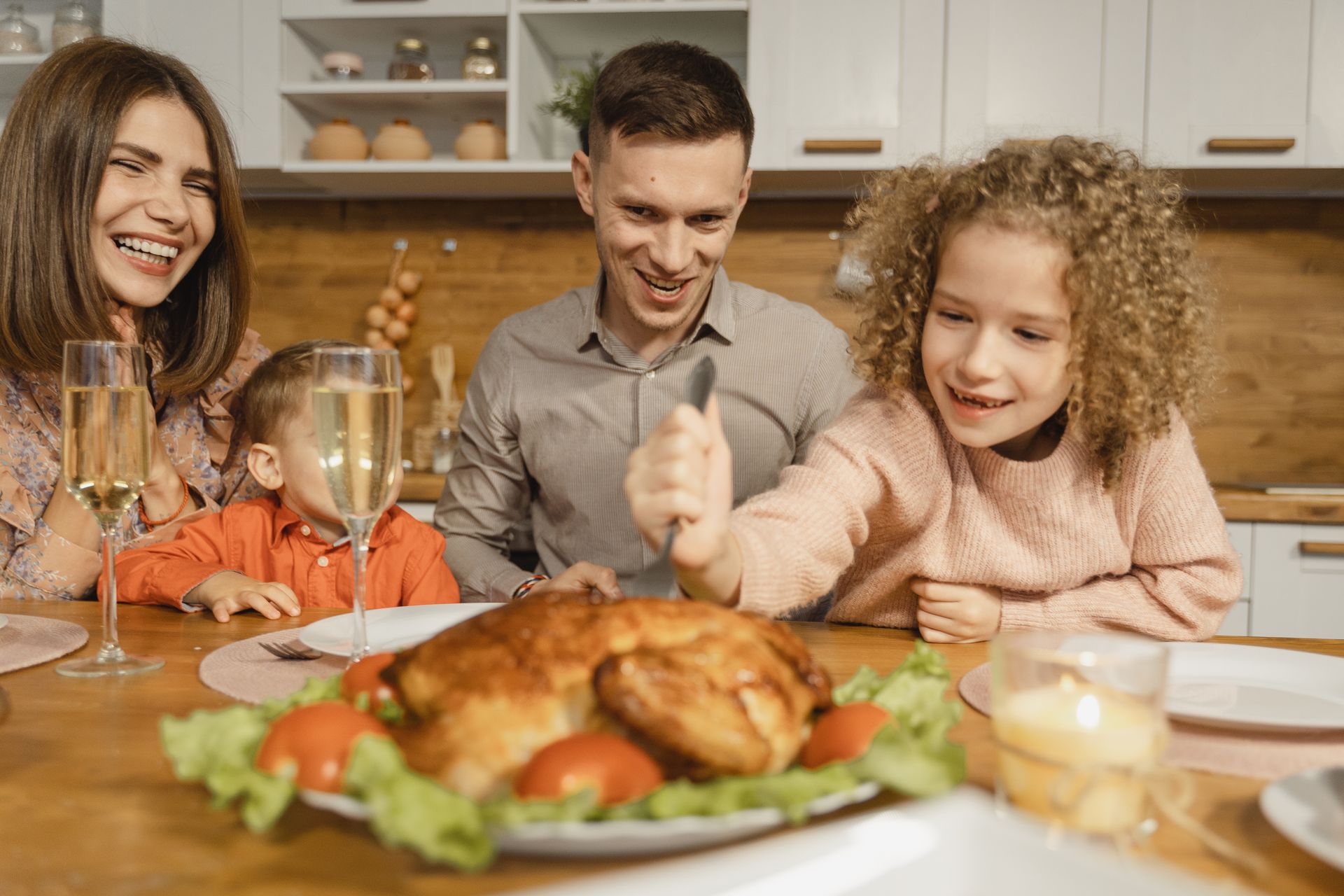 Family laughing around the dinner table with a roast chicken, the kind of dinner that goes on the calendar first